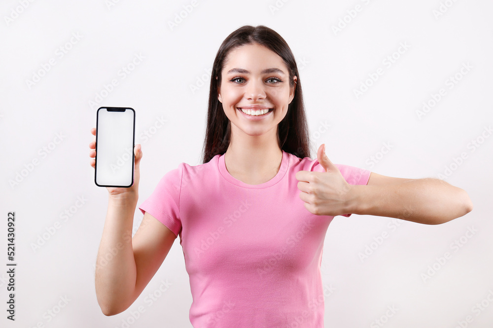 Young beautiful brunette woman wearing pink t-shirt posing with a phone over isolated white background. Portrait of female model showing blank screen cellphone. Close up, copy space. Young beautiful brunette woman wearing pink t-shirt posing with a phone over isolated white background. Portrait of female model showing blank screen cellphone. Close up, copy space.