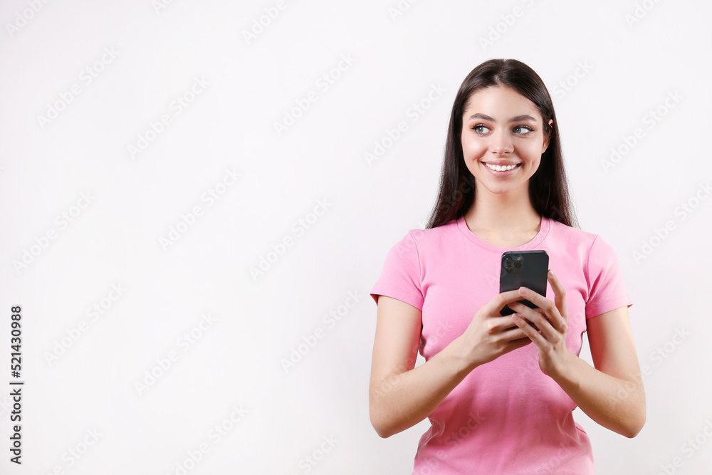 Portrait of young brunette woman wearing pink t-shirt texting on the phone over isolated white background. Joyful female holding a smartphone. Copy space for text, background, close up. Portrait of young brunette woman wearing pink t-shirt texting on the phone over isolated white background. Joyful female holding a smartphone. Copy space for text, background, close up.