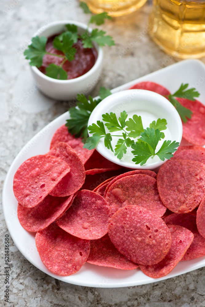Close-up of red potato chips with dipping sauces, vertical shot on a light-brown granite background