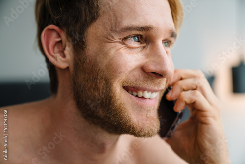 Young shirtless man using cellphone while sitting in bed at home