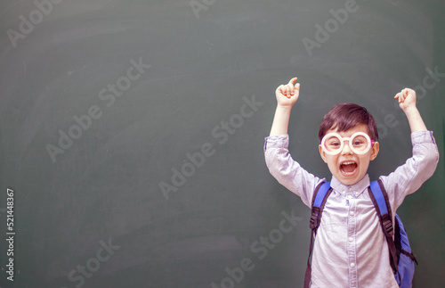 happy kid with party decorative glasses pointing indicates on empty no text green color blackboard .smiling child pointing with hand finger at empty space, raised hands hooray emotion.back to school 