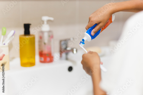 Boy hand putting toothpaste on toothbrush in the bathroom.
