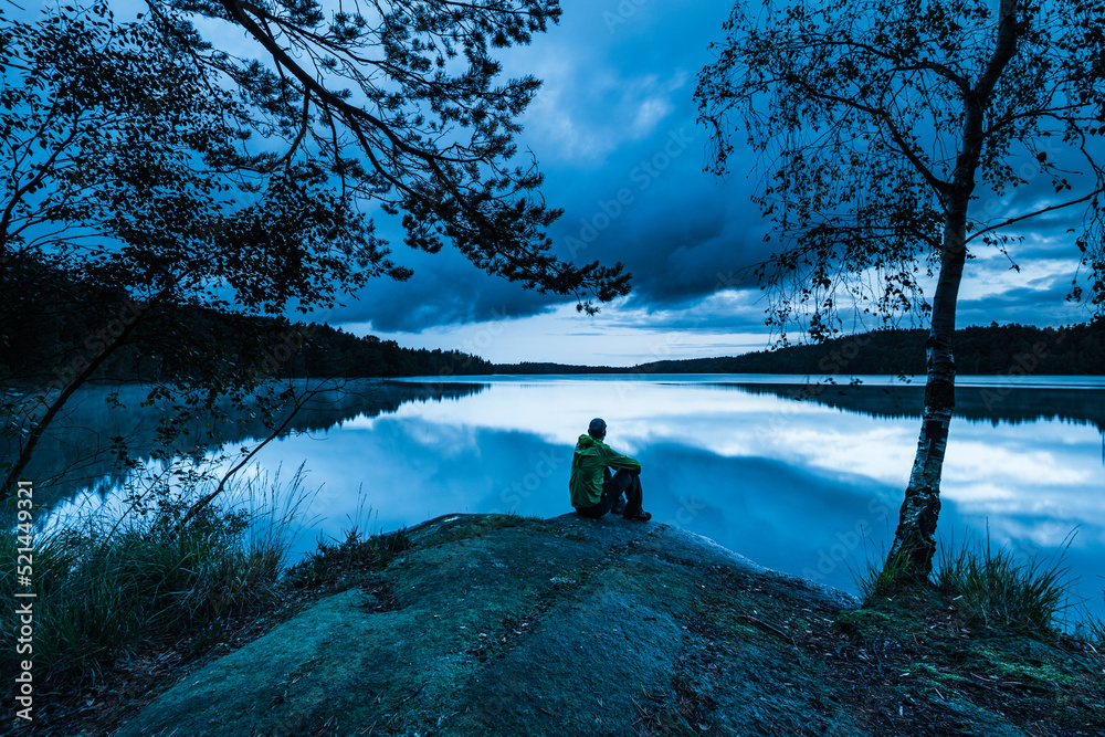 Lonely man sitting besides lake at blue hour