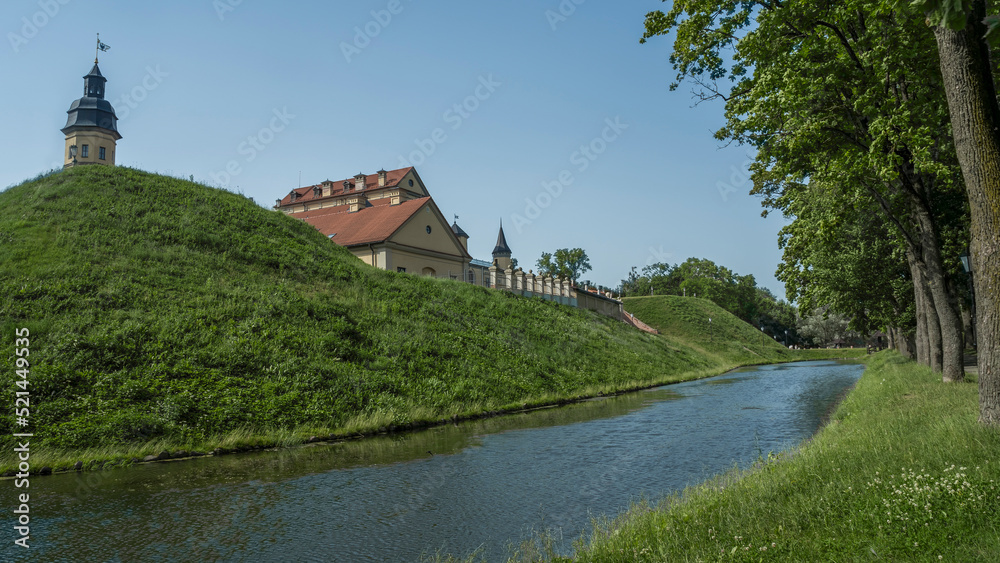 Moat of old castle. Moat with reflection in the water and trees. Sunny summer day. Palace, tower, corner towers and moat.