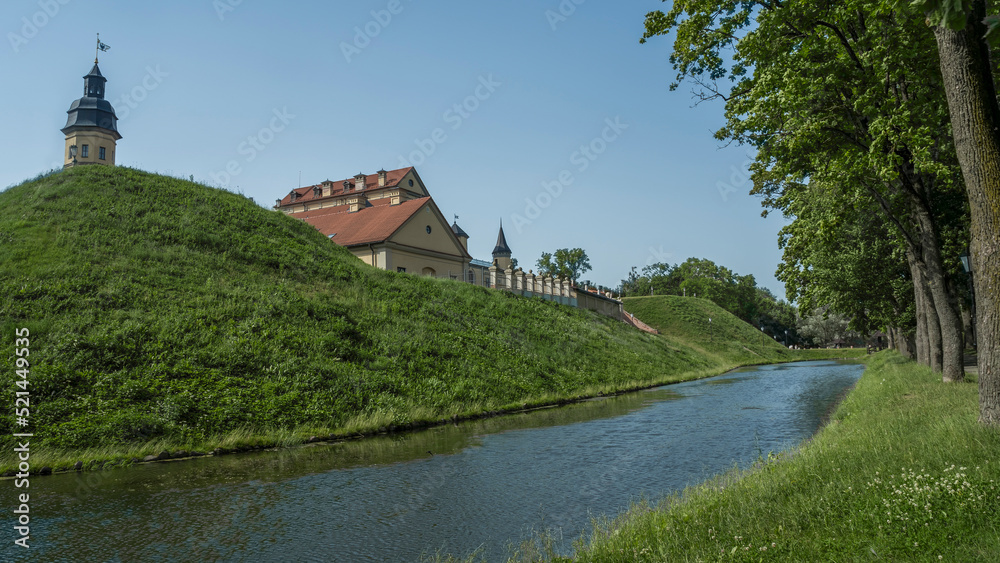 Naklejka premium Moat of old castle. Moat with reflection in the water and trees. Sunny summer day. Palace, tower, corner towers and moat.