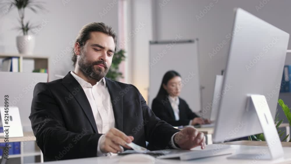 Confident caucasian boss sitting at open space office with dollar banknotes on table. Happy bearded man in suit feeling satisfaction from productive financial agreement. Confident caucasian boss sitting at open space office with dollar banknotes on table. Happy bearded man in suit feeling satisfaction from productive financial agreement.