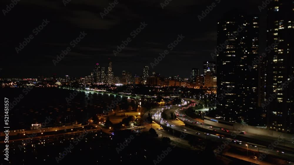 Aerial drone shot of traffic movement over a bridge along the seaside with the view of high-rise office and residential buildings in the background in Chicago, USA at night time. Aerial drone shot of traffic movement over a bridge along the seaside with the view of high-rise office and residential buildings in the background in Chicago, USA at night time.
