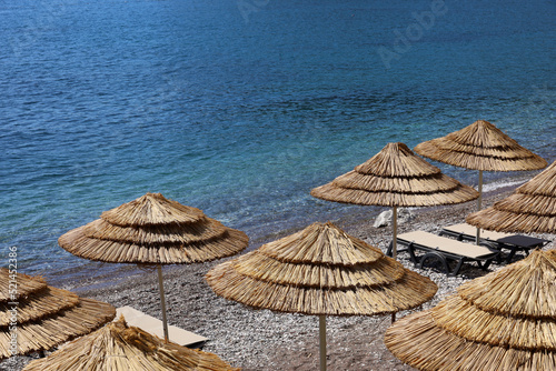 Fototapeta Naklejka Na Ścianę i Meble -  Empty pebble beach with wicker parasols and lounge chairs. Picturesque view to sea with blue water, summer resort