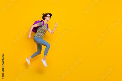 Full length photo of sweet excited lady wear striped t-shirt spectacles backpack running fast empty space isolated yellow color background