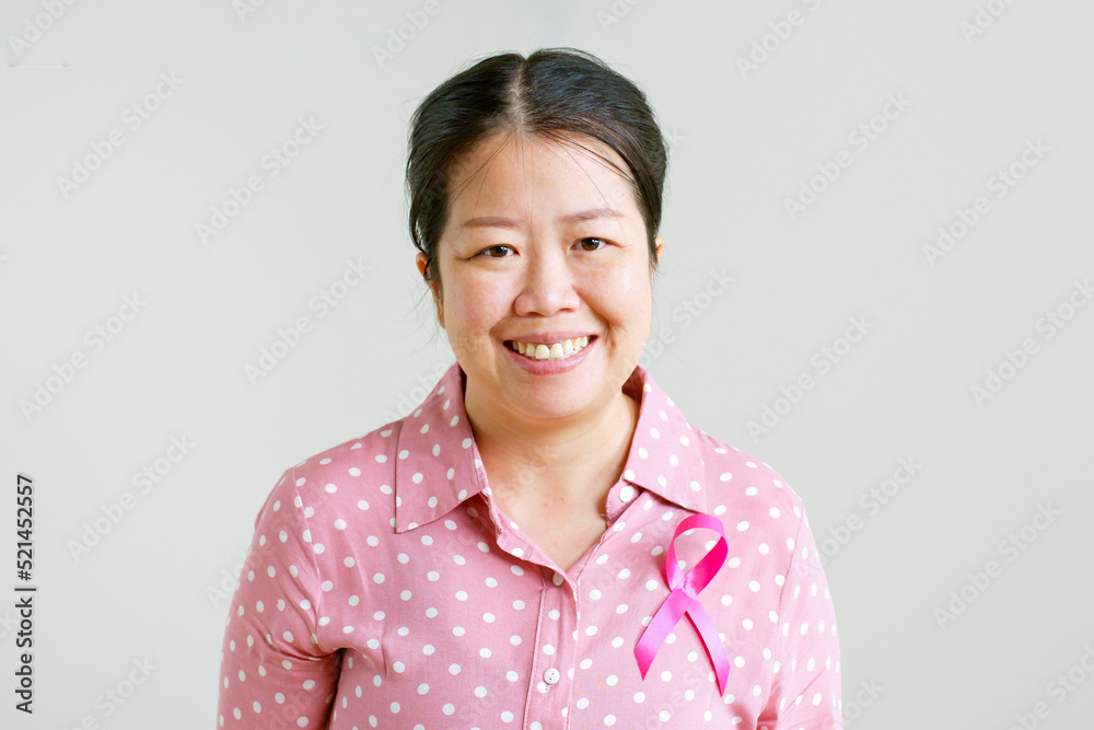 Portrait of young Asian woman in pink shirt with pink ribbon smiling on gray background for October breast cancer awareness month Portrait of young Asian woman in pink shirt with pink ribbon smiling on gray background for October breast cancer awareness month