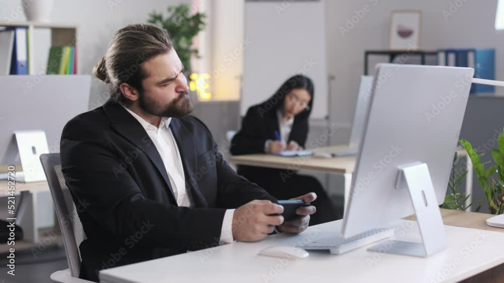 Bearded caucasian office worker using modern smartphone for playing work during coffee break at office. Handsome man in suit feeling anger because of losing. Bearded caucasian office worker using modern smartphone for playing work during coffee break at office. Handsome man in suit feeling anger because of losing.
