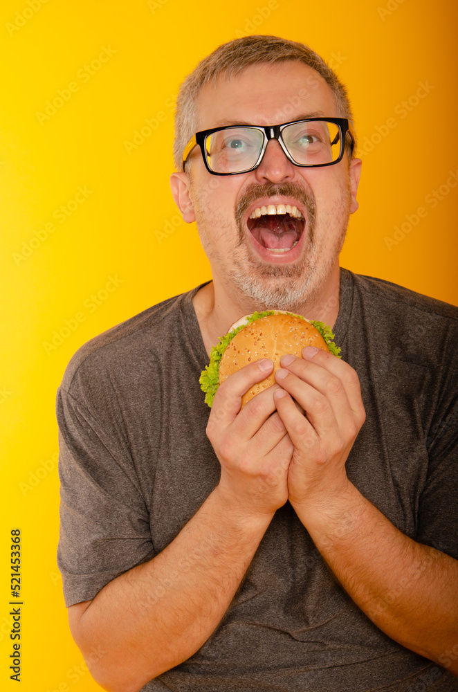 a man with a gray haired man happily holds a burger in his hands with a tantrum to see him in glasses