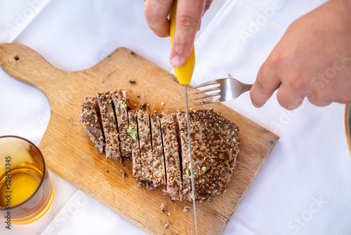 hands cutting a ppper steak on wooden plate