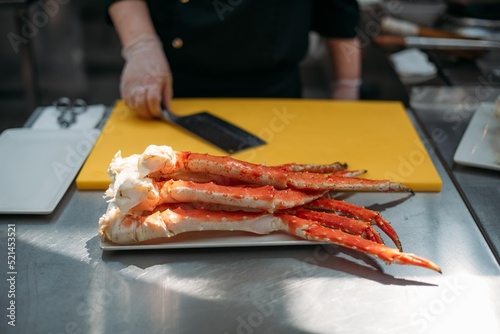 The legs of a fresh red Kamchatka crab on the table and the hands of a chef with a knife in the restaurant kitchen. photo