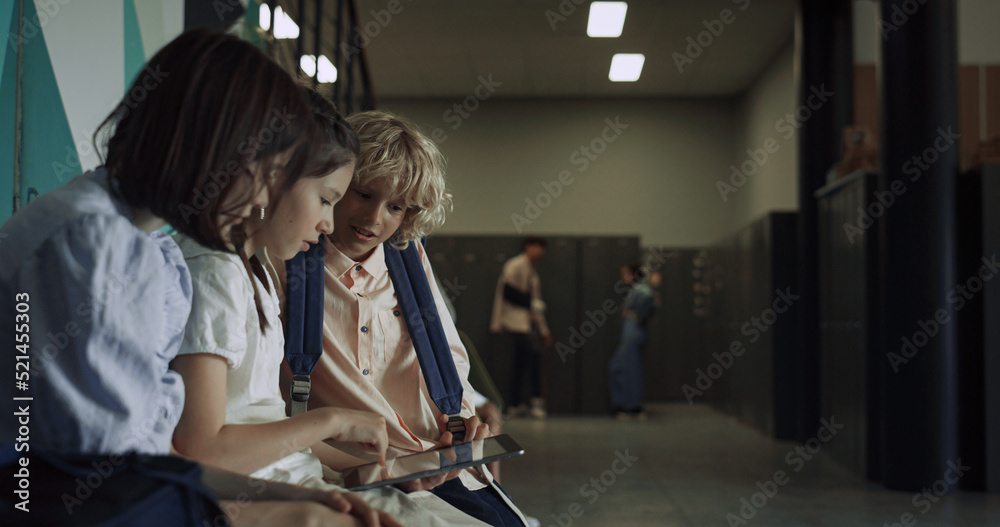 Three focused students sitting with tablet in school hall. Preteen communication