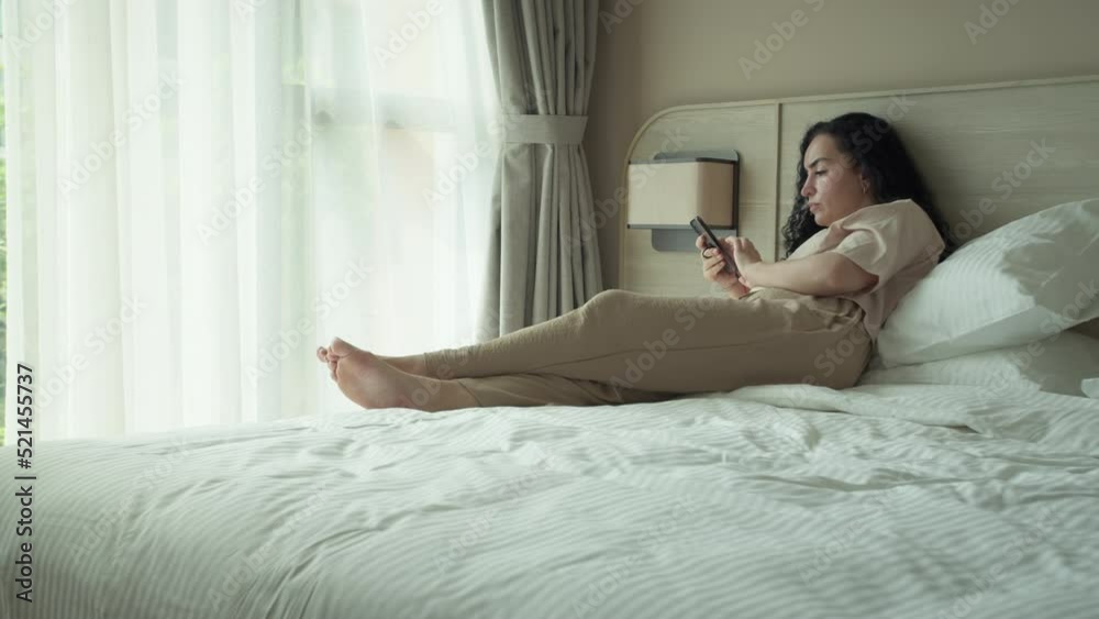 Worried woman using app on cellphone at home. Beautiful girl relaxing while chatting on mobile phone and looking at phone. Thoughtful young caucasian woman using smartphone while sitting on bedroom. Worried woman using app on cellphone at home. Beautiful girl relaxing while chatting on mobile phone and looking at phone. Thoughtful young caucasian woman using smartphone while sitting on bedroom.