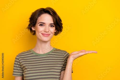 Closeup photo of young funny smiling cute woman holds hand promotion empty space new product isolated on yellow color background