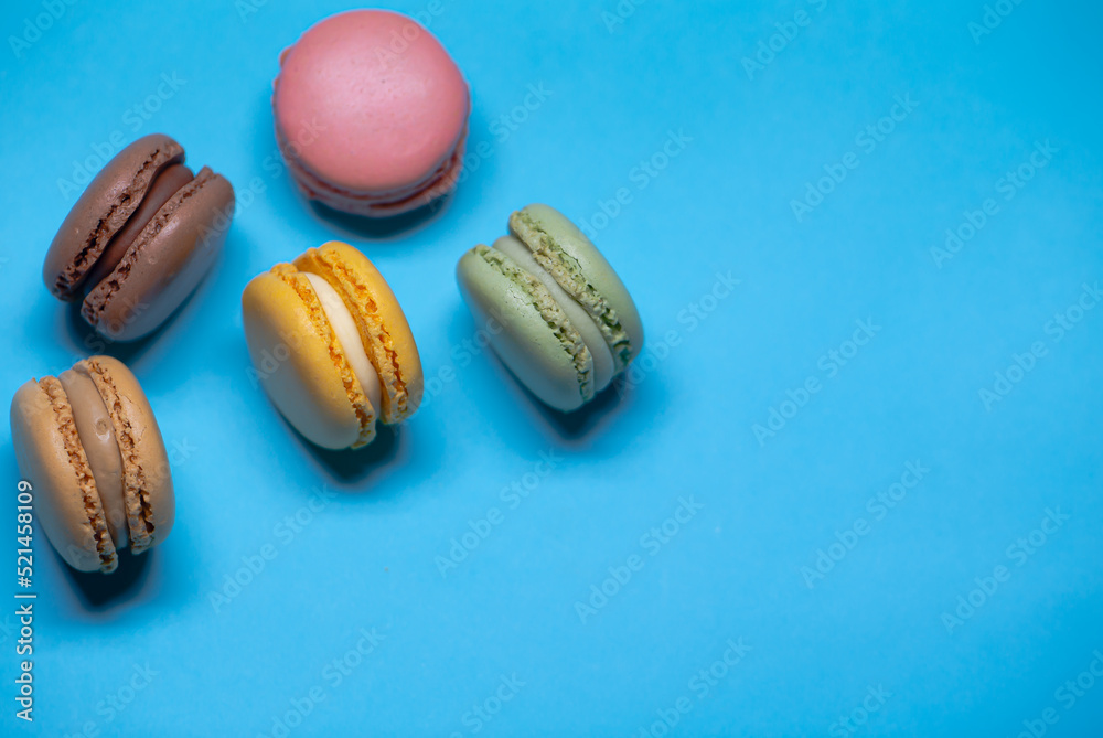 Macarons. French colored cookies filled with cream on a blue background. Photo on one side. Sweets with sugar. Cream filled sweets. Pasta for tea. Macarons. French colored cookies filled with cream on a blue background. Photo on one side. Sweets with sugar. Cream filled sweets. Pasta for tea.