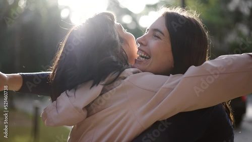 Two happy female best friends hugging each other. Women embrace reunion outdoors at park photo
