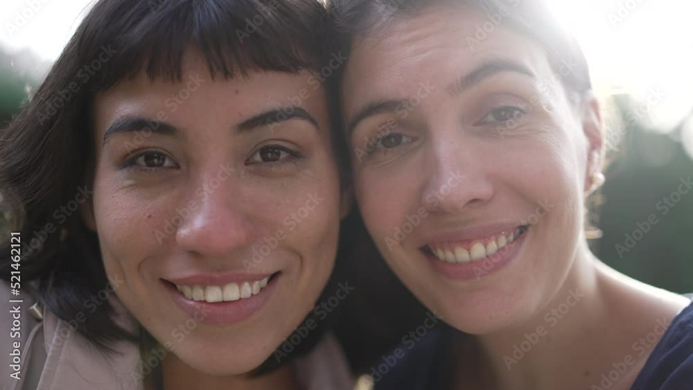 Two young women faces together cheek to cheek. Portrait of diverse people looking at camera with sunlight Two young women faces together cheek to cheek. Portrait of diverse people looking at camera with sunlight