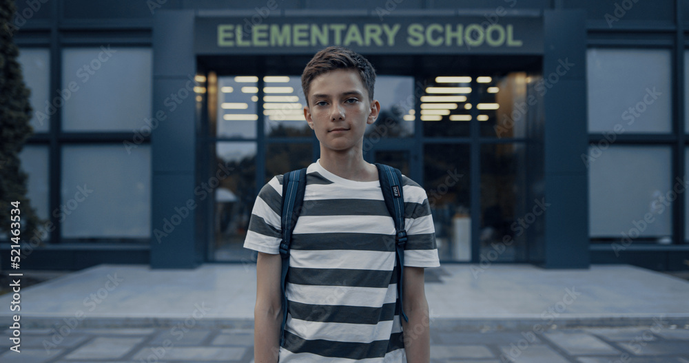 Closeup serious teen boy standing at schoolyard. Tensed schoolboy posing alone.