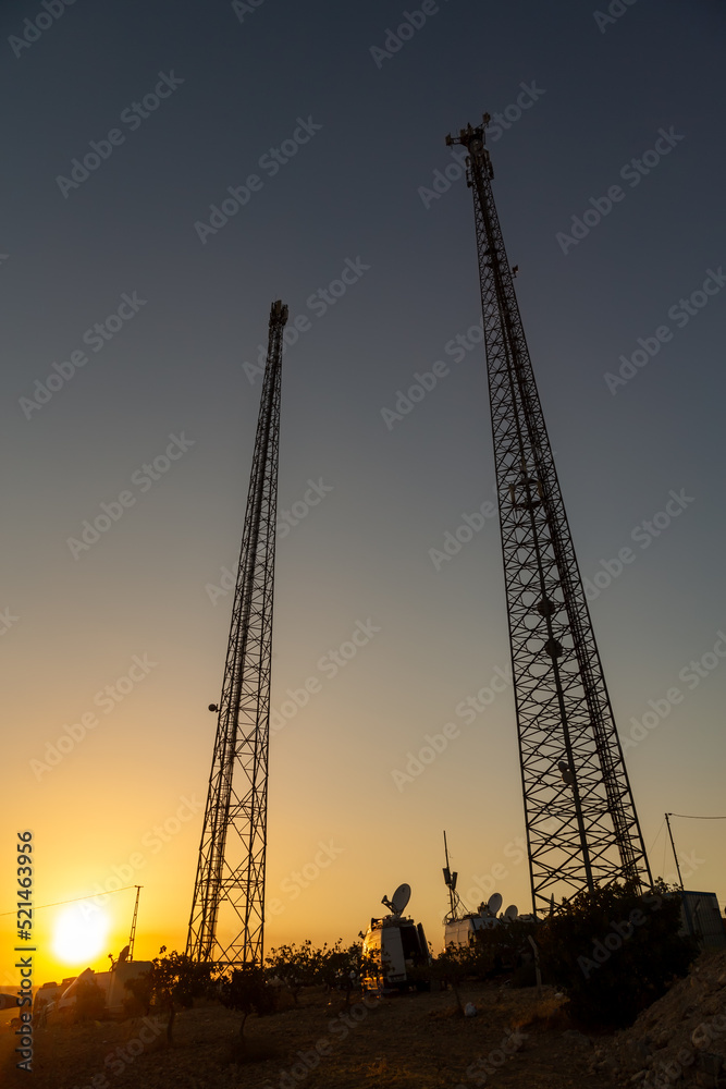 Global System for Mobile Communications cellular base stations silhouettes against an impressive summer sunset background.