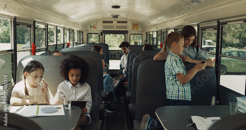 Teen classmates sitting schoolbus talking. Multicultural class chatting playing.