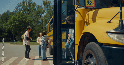 Two pupils leaving schoolbus chatting. Teenagers standing talking near bus.