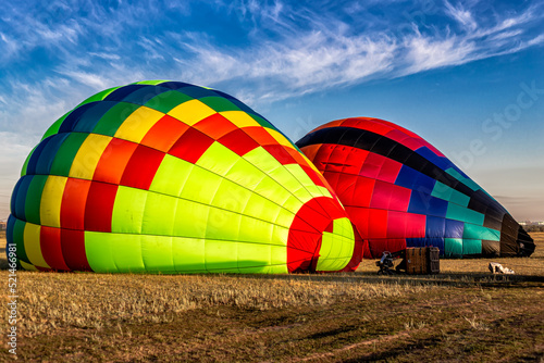 two hot air balloons lie on the ground in the grass and are inflated with hot air in preparation for flight through the sky