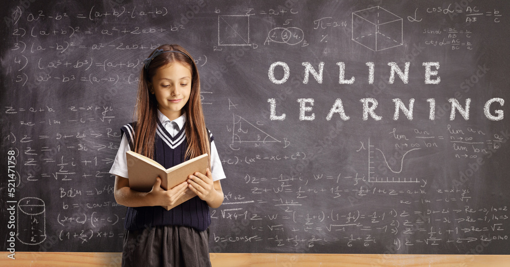 Schoolgirl reading a book in front of a chalkboard with text online learning Schoolgirl reading a book in front of a chalkboard with text online learning