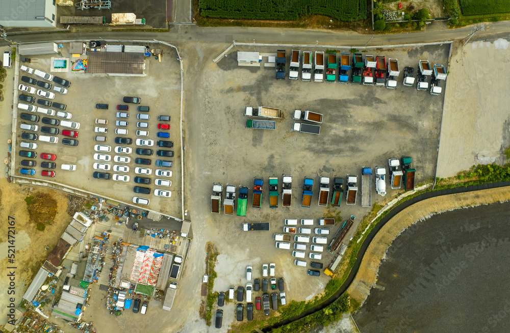 Top down aerial view of lifting dump trucks and work vehicles in dirt lot outdoors