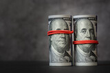 Rolls of hundred-dollar bills with red rubber bands on them, covering mouth and eyes of Franklin's image. The concept is people can turn a blind eye and remain silent for money; bribes, corruption.