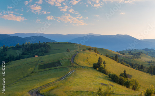 A wide-angle view of green mountain hills after the rain in sunset light in the Carpathian mountains in the summer. Panorama of green grass hills with rural buildings.