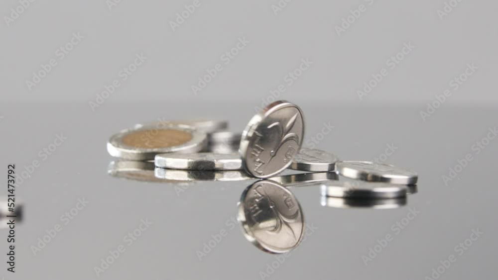 New Israeli Shekels coins falling in slow motion on a reflective surface