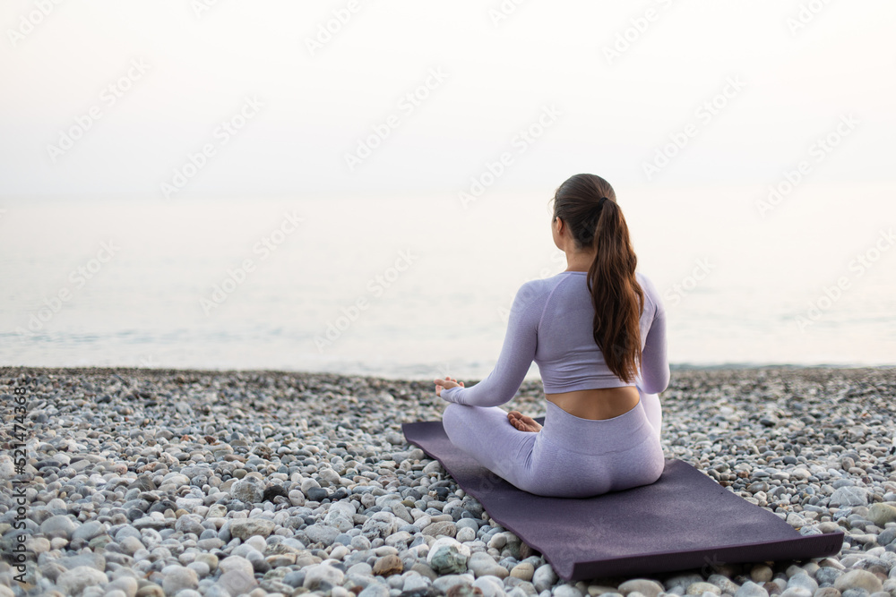 Young woman practice yoga and meditation near the sea at sunrise, healthy lifestyle concept, lotus position back view
