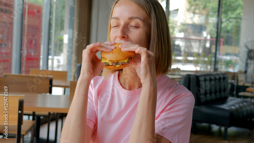 Young woman eating fast food  hamburger in cafe  close-up