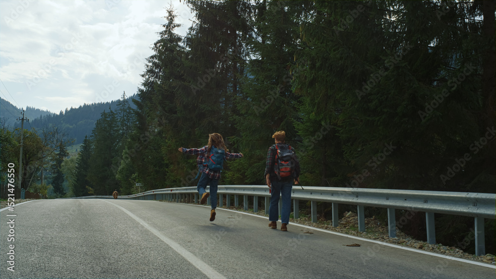 Friends trekking mountains road in forest nature. Couple wear backpacks outside.