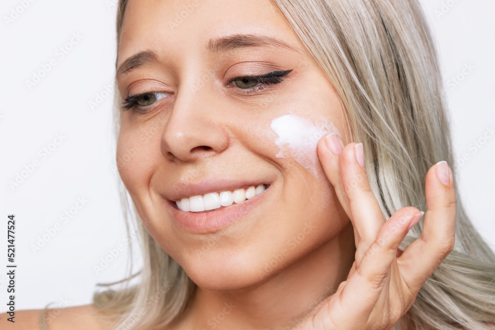 Close up of a young caucasian blonde woman touching the face with her hand applying a cream on the skin isolated on a white background. Nourishing moisturizing cream. Cosmetology and beauty concept Close up of a young caucasian blonde woman touching the face with her hand applying a cream on the skin isolated on a white background. Nourishing moisturizing cream. Cosmetology and beauty concept