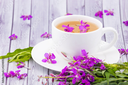 Still life of fireweed herbal tea in white ceramic cup with fresh purple great willowherb flowers against wooden background.Herbal medicine concept.Tea from fermented Chamaenerion angustifolium leaves