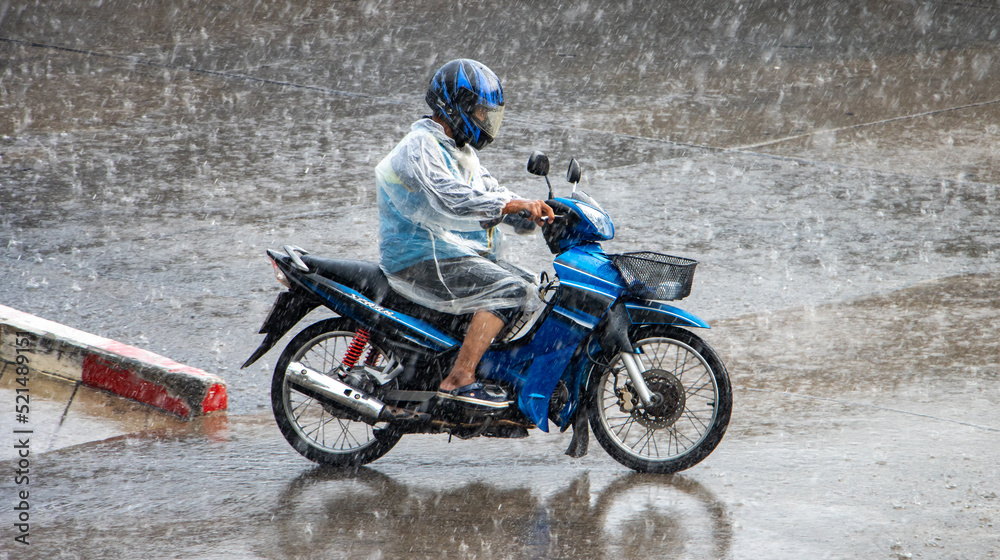 A motorcycle taxi driver rides in a heavy rain on a motorcycle