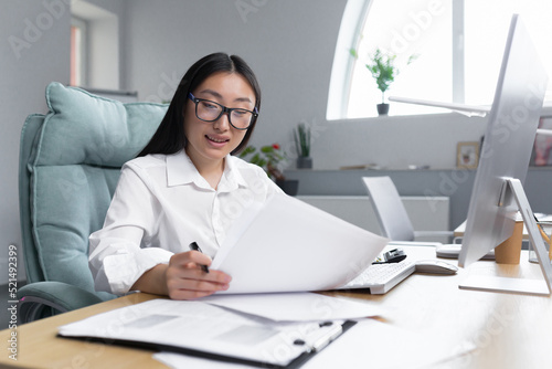 Work with documents. Portrait of a young beautiful business woman Asian accountant works with documents and reports. Sitting at the desk in the office, writing.