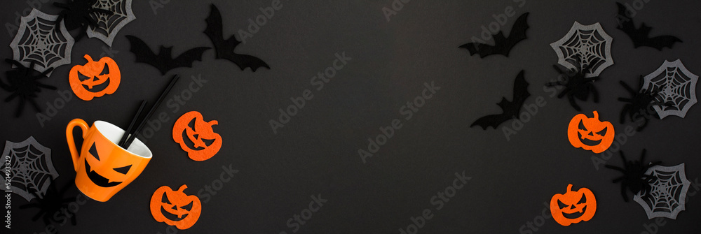Halloween background. Orange cup, decorative spiders, pumpkins, spider webs and bats on the black background. Copy space. Top view. Halloween background. Orange cup, decorative spiders, pumpkins, spider webs and bats on the black background. Copy space. Top view.