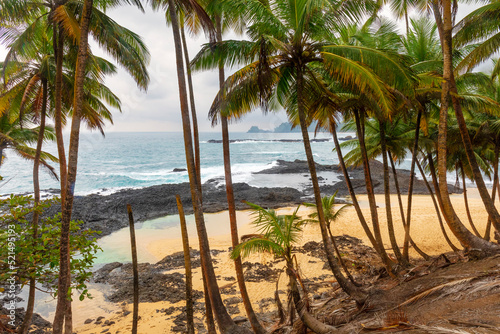 Coconut trees leaning over a sandy beach framed by dark gray volcanic rocks which protect it from the ocean beyond.