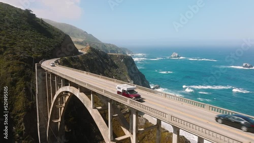 People traveling in camper van by scenic ocean route by American West Coast. Tourists exploring California shore in Big Sur park with cinematic landscapes and beautiful nature. Aerial bridge traffic