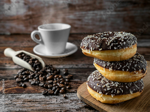 Fresh donuts with hot coffee, a wooden spoon full of coffee beans, warm colors, wooden background, breakfast, snack.