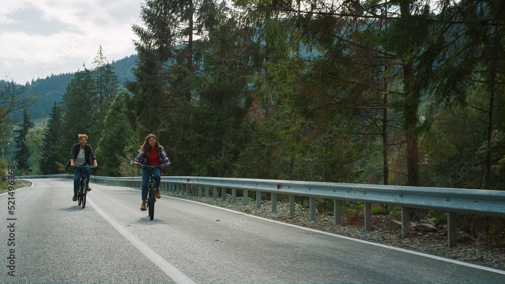 Couple cycling mountain road together in forest landscape. Tourists riding bike.