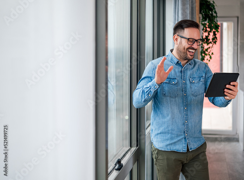 Smiling entrepreneur waving while video conferencing on digital tablet by the window.