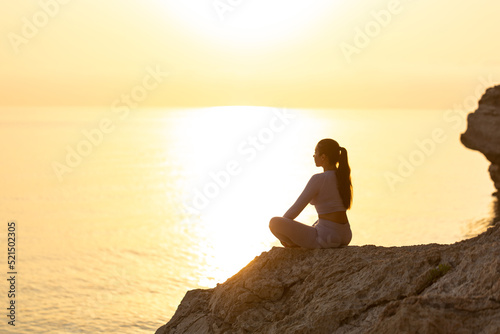 silhouette of young woman practice yoga and meditation near the sea at sunrise, healthy lifestyle concept, lotus position © uv_group
