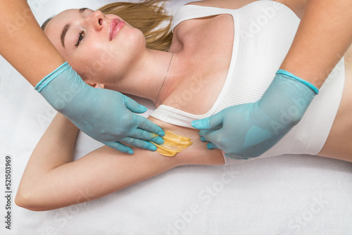 Depilation and epilation of the female armpit with liquid sugar paste. The beautician's hand applies wax paste to the armpit. © Tania