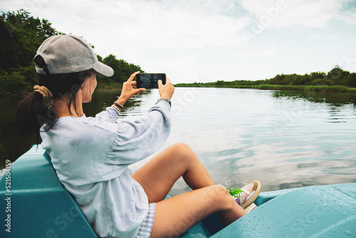 Young caucasian tourist woman sit in paddle boat and take photo of lake and green nature in Kolkheti, Georgia